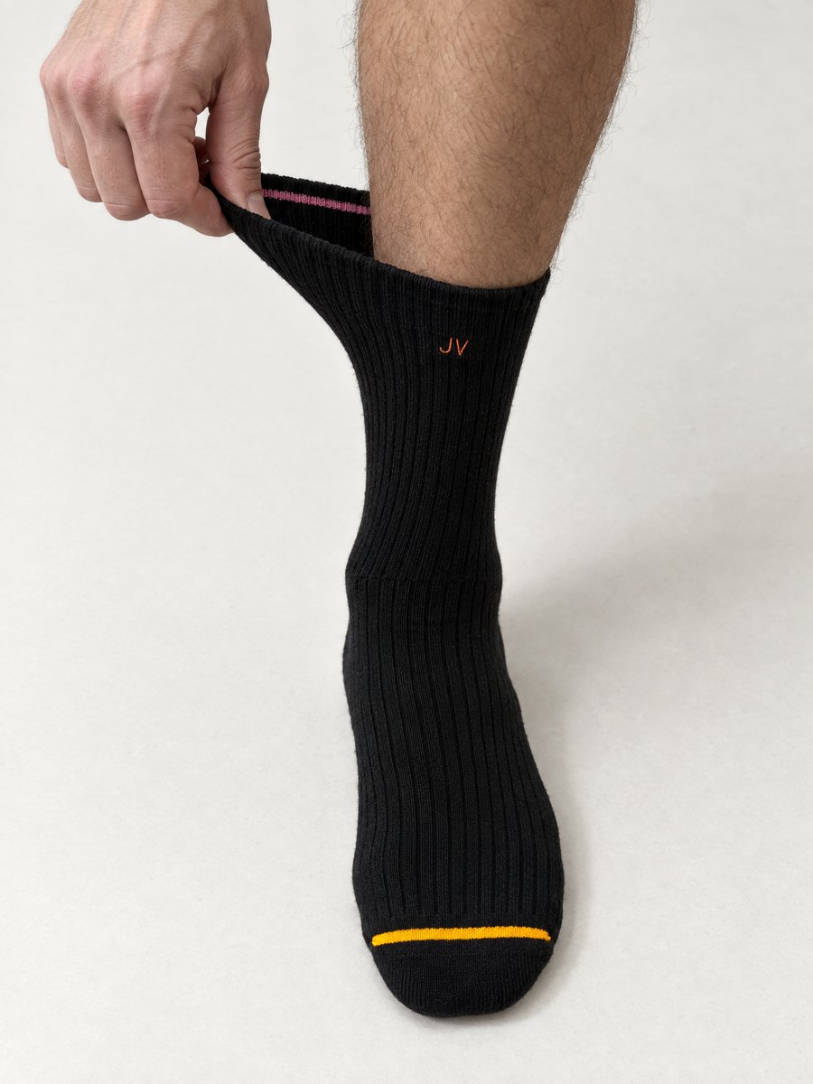 A hand pulls the cuff of a black KINJO 01 sock wide while it is worn, and the ribbed knit stretches with it