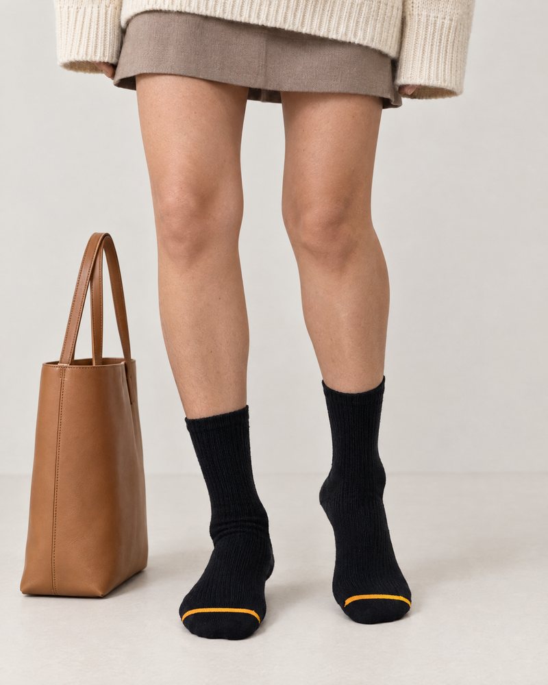 Black pair worn with a skirt and jumper, a tote bag beside her, ready for class